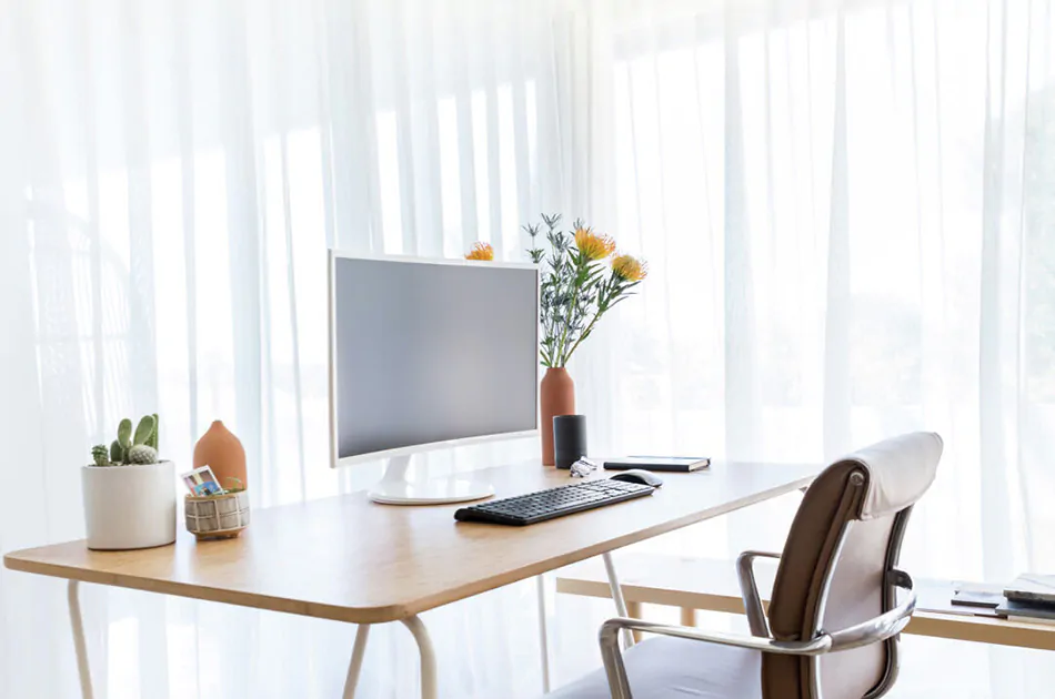 A home office with sheer curtains filtering natural light on a desk.